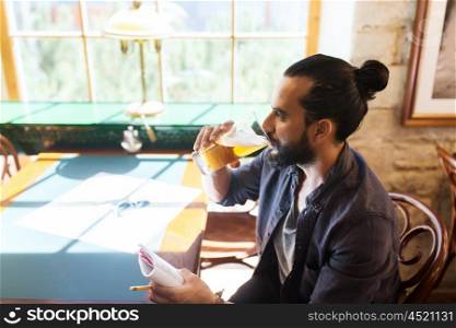 people, drinks, alcohol and leisure concept - happy young man with notebook drinking beer at bar or pub