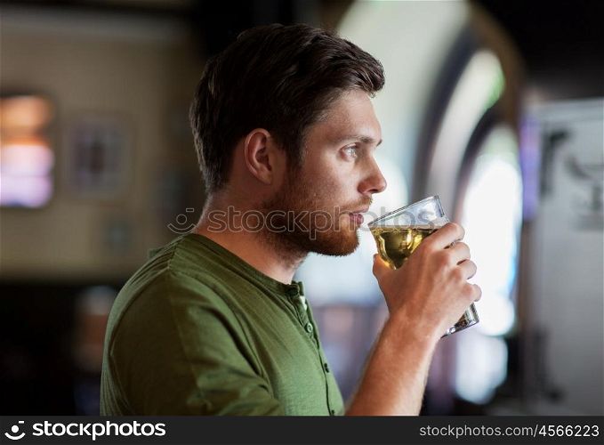 people, drinks, alcohol and leisure concept - young man drinking beer at bar or pub