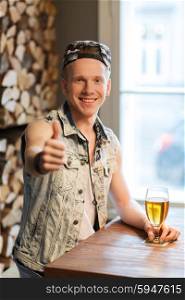 people, drinks, alcohol, gesture and leisure concept - happy young man drinking beer and showing thumbs up at bar or pub