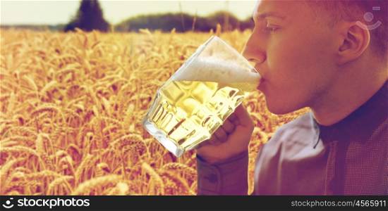 people, drinks and alcohol concept - close up of young man drinking beer from glass mug over cereal field background