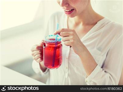 people, drinks and holidays concept - close up of happy woman drinking juice from glass mug with straw at home