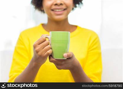 people, drinks and leisure concept - close up of happy african american woman drinking tea from cup or mug at home