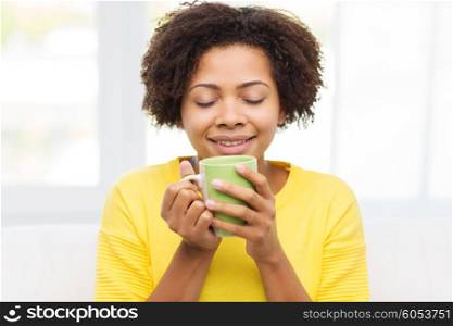 people, drinks and leisure concept - happy african american woman drinking tea from cup or mug at home