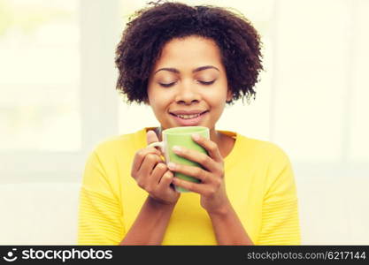 people, drinks and leisure concept - happy african american woman drinking tea from cup or mug at home