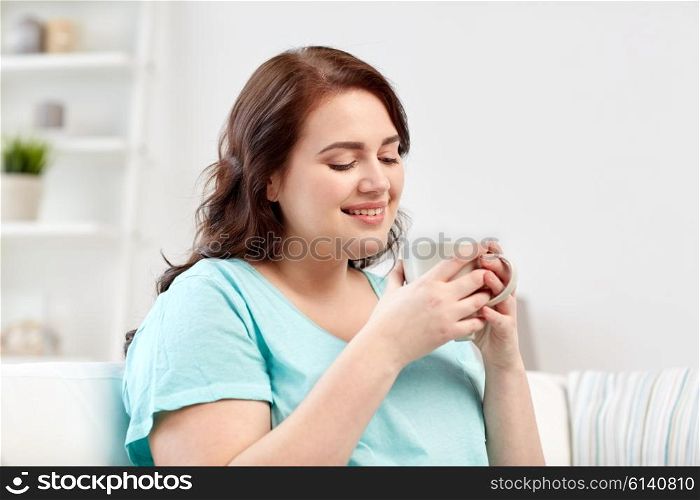 people, drinks and leisure concept - happy plus size young woman with cup of tea at home
