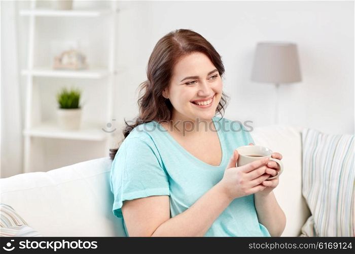 people, drinks and leisure concept - happy plus size young woman with cup of tea at home