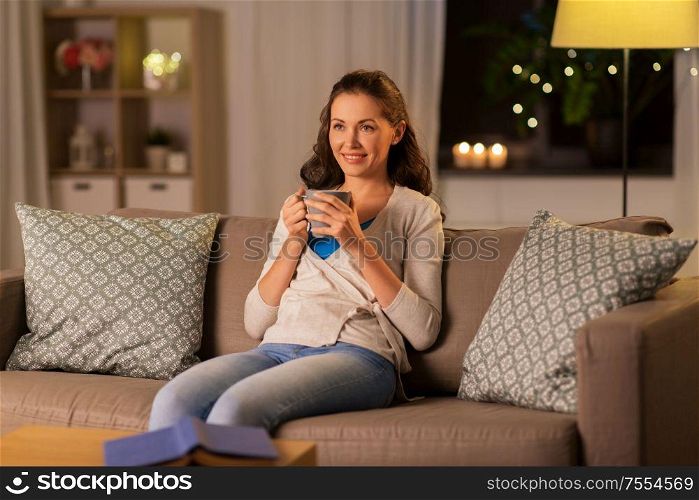 people, drinks and leisure concept - happy woman with mug drinking tea or coffee at home in evening. happy woman drinking tea or coffee at home
