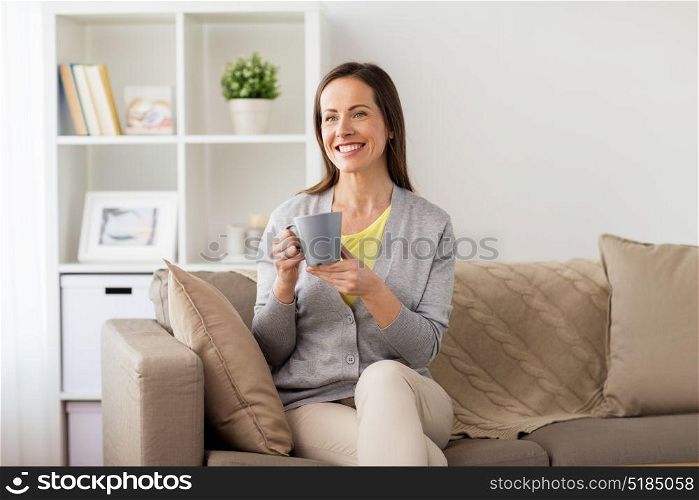 people, drinks and leisure concept - happy woman with mug drinking tea or coffee at home. happy woman drinking tea or coffee at home