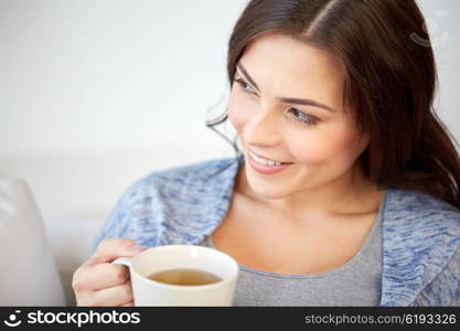 people, drinks and leisure concept - happy young woman with cup of tea at home