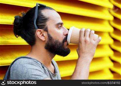 people, drinks and lifestyle concept - man drinking coffee from disposable paper cup on street over ribbed yellow wall background. man drinking coffee from paper cup over wall