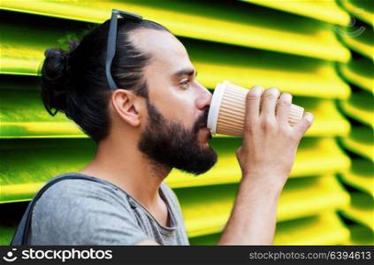 people, drinks and lifestyle concept - man drinking coffee from disposable paper cup on street over ribbed green wall background. man drinking coffee from paper cup over wall