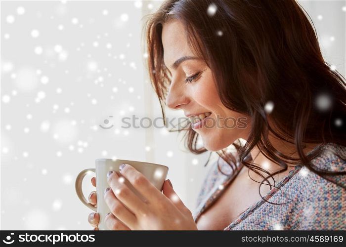 people, drinks, christmas and winter concept - close up of happy young woman with cup of tea or coffee at home over snow