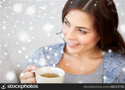 people, drinks, christmas and winter concept - happy young woman with cup of tea at home over snow