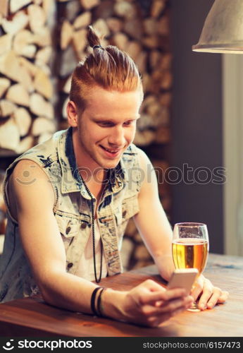 people, drinks, technology and leisure concept - happy young man with smartphone drinking beer at bar or pub