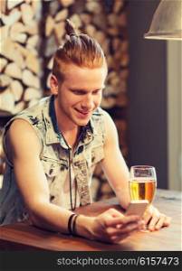 people, drinks, technology and leisure concept - happy young man with smartphone drinking beer at bar or pub