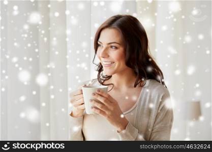 people, drinks, winter and christmas concept - happy young woman with cup of tea or coffee at home over snow