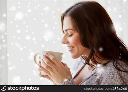 people, drinks, winter, christmas and bliss concept - happy young woman with cup of tea or coffee at home over snow