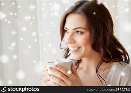 people, drinks, winter, christmas and leisure concept - close up of happy young woman with cup of tea or coffee at home over snow