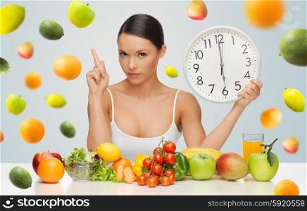 people, eating and diet concept - woman with healthy food holding big clock, pointing finger up and warning over gray background with falling fruits