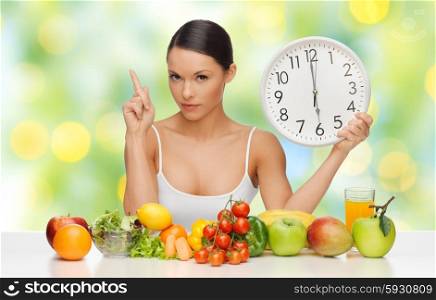 people, eating and diet concept - woman with healthy food holding big clock, pointing finger up and warning over green lights background