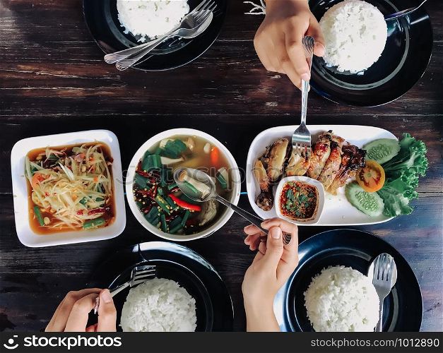 People eating Thai food on a brown wooden table.