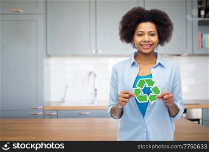 people, ecology and environment concept - happy african american young woman with recycling symbol over kitchen background. happy young woman with recycling sign on kitchen