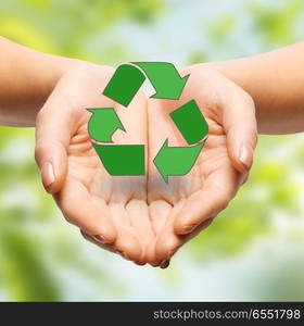 people, ecology, environment and conservation concept - close up of hands holding green recycling sign over natural background. close up of hands holding green recycling sign. close up of hands holding green recycling sign