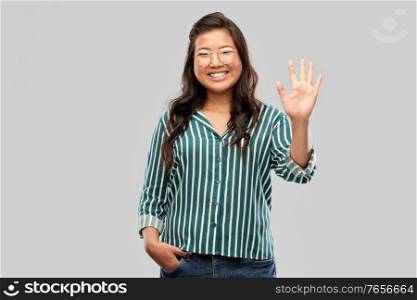 people, education and school concept - happy asian woman in glasses or student waving hand over grey background. happy asian woman in glasses waving hand
