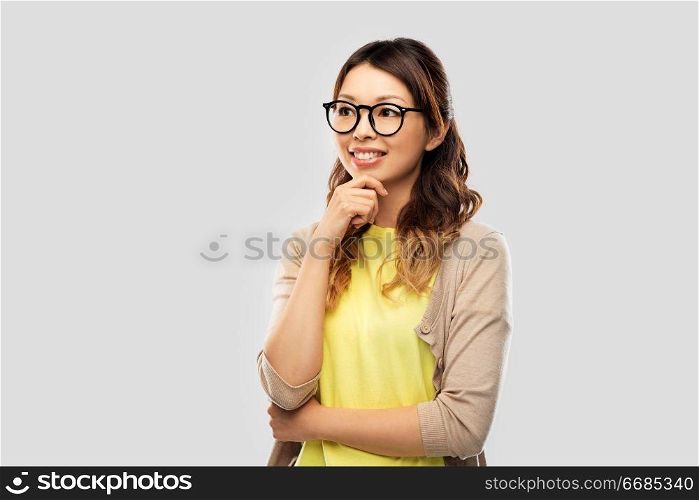 people, education and school concept - happy asian woman in glasses or student over grey background. happy asian woman in glasses or student