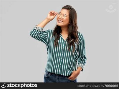 people, education and school concept - happy asian woman in glasses or student over grey background. happy asian woman in glasses or student