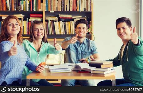 people, education, gesture and school concept - group of happy students with books showing thumbs up and preparing to exam in library