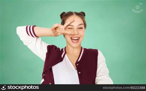 people, education, gesture and teens concept - happy smiling pretty teenage student girl showing peace sign and winking over green school chalk board background