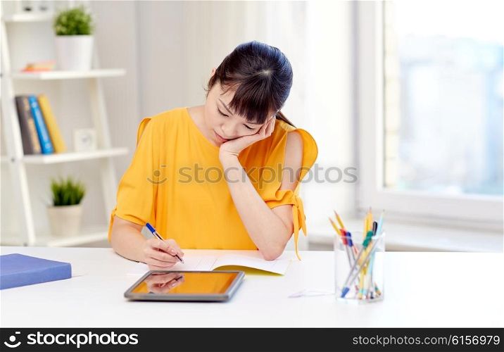 people, education, high school and learning concept - bored asian young woman student with tablet pc computer, book and notepad writing at home