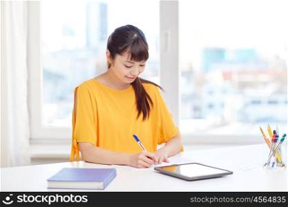 people, education, high school and learning concept - happy asian young woman student with tablet pc computer, book and notepad writing at home