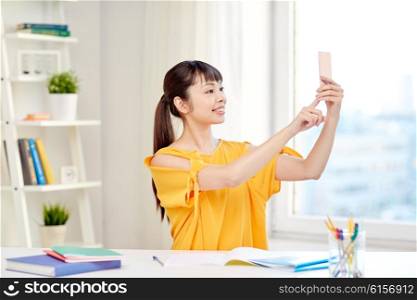 people, education, high school and learning concept - happy asian young woman student taking selfie with smartphone at home