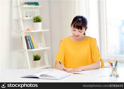 people, education, high school and learning concept - happy asian young woman student with book and notepad writing at home