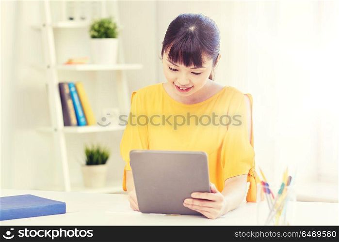 people, education, high school and learning concept - happy asian young woman student with tablet pc computer, book and notepad writing at home. asian woman student with tablet pc at home