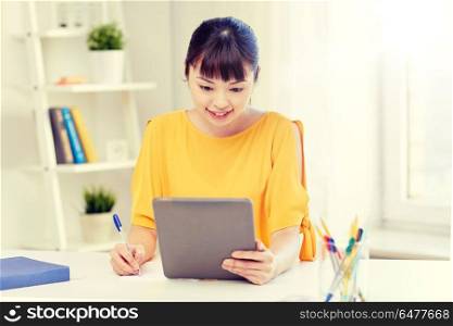 people, education, high school and learning concept - happy asian young woman student with tablet pc computer, book and notepad writing at home. asian woman student with tablet pc at home. asian woman student with tablet pc at home