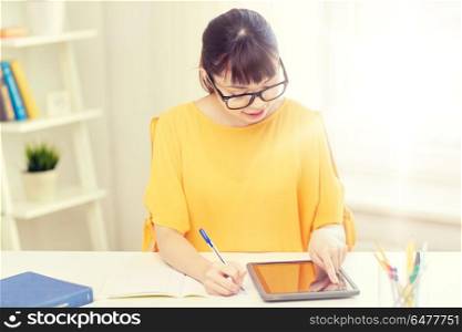 people, education, high school and learning concept - happy asian young woman student in glasses with tablet pc computer, book and notepad writing at home. asian woman student with tablet pc at home. asian woman student with tablet pc at home
