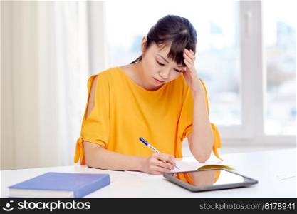people, education, high school and learning concept - tired or bored asian young woman student with tablet pc computer, book and notepad writing at home