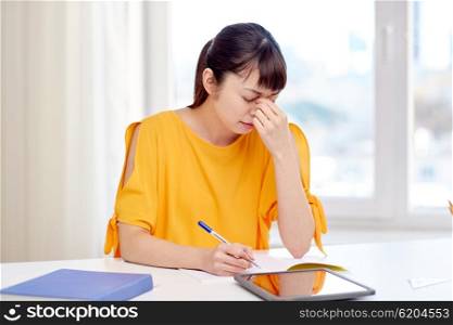 people, education, high school and learning concept - tired or stressed asian young woman student with tablet pc computer, book and notepad writing at home