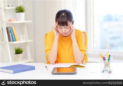 people, education, high school, stress and learning concept - tired asian young woman student with tablet pc computer and notepad suffering from headache at home