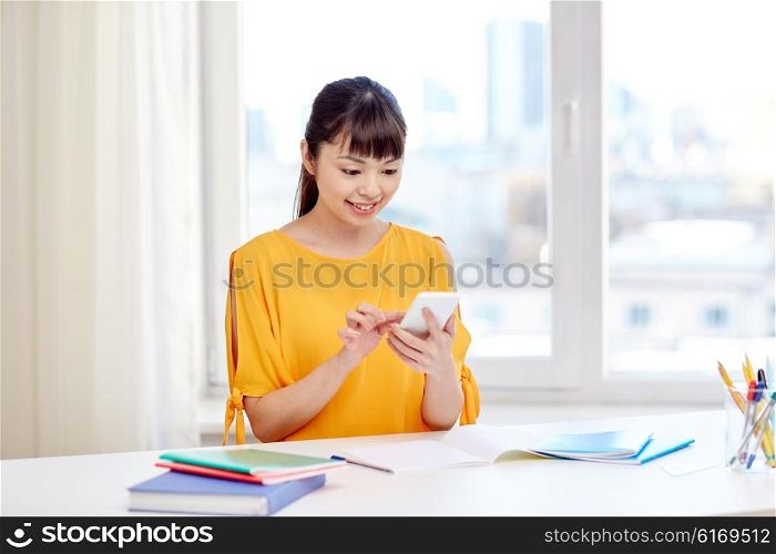 people, education, high school, technology and learning concept - happy asian young woman student with smartphone texting message at home