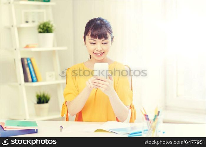people, education, high school, technology and learning concept - happy asian young woman student with smartphone texting message at home. happy young woman student with smartphone at home. happy young woman student with smartphone at home