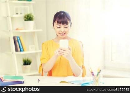 people, education, high school, technology and learning concept - happy asian young woman student with smartphone texting message at home. happy young woman student with smartphone at home. happy young woman student with smartphone at home