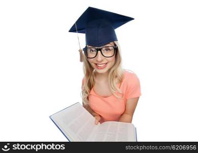people, education, knowledge and graduation concept - smiling young student woman in mortarboard and eyeglasses with encyclopedia book