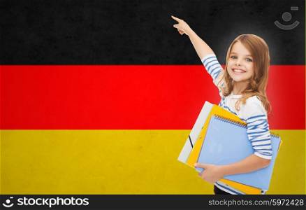 people, education, learning and school concept - happy student girl with folders pointing finger over german flag background