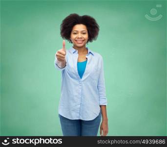 people, education, school and gesture concept - happy afro american young woman showing thumbs up over green chalk board background. happy afro american woman showing thumbs up