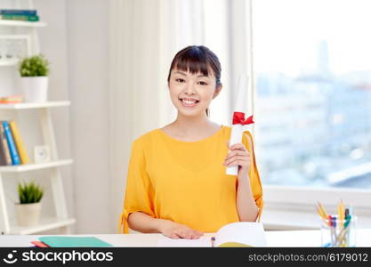 people, education, school, graduation and learning concept - happy asian young woman student with diploma scroll at home