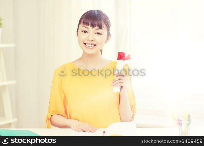 people, education, school, graduation and learning concept - happy asian young woman student with diploma scroll at home. happy asian woman student with diploma at home